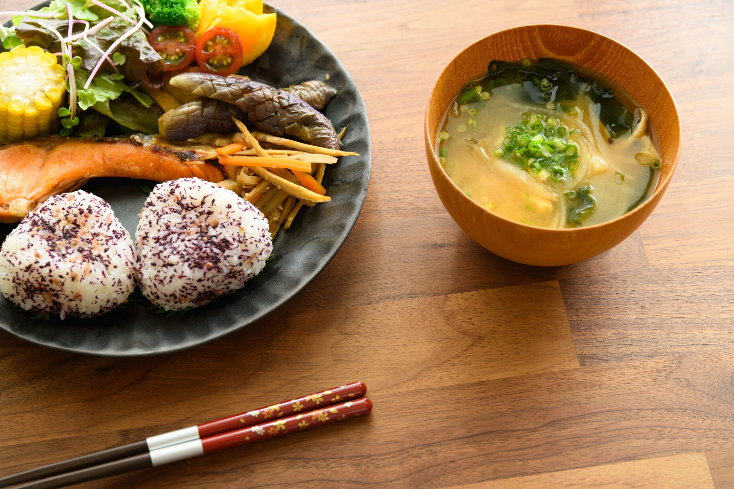 おにぎりや茄子の煮びたし、きんぴらなどの和食が乗った丸い皿と味噌汁。