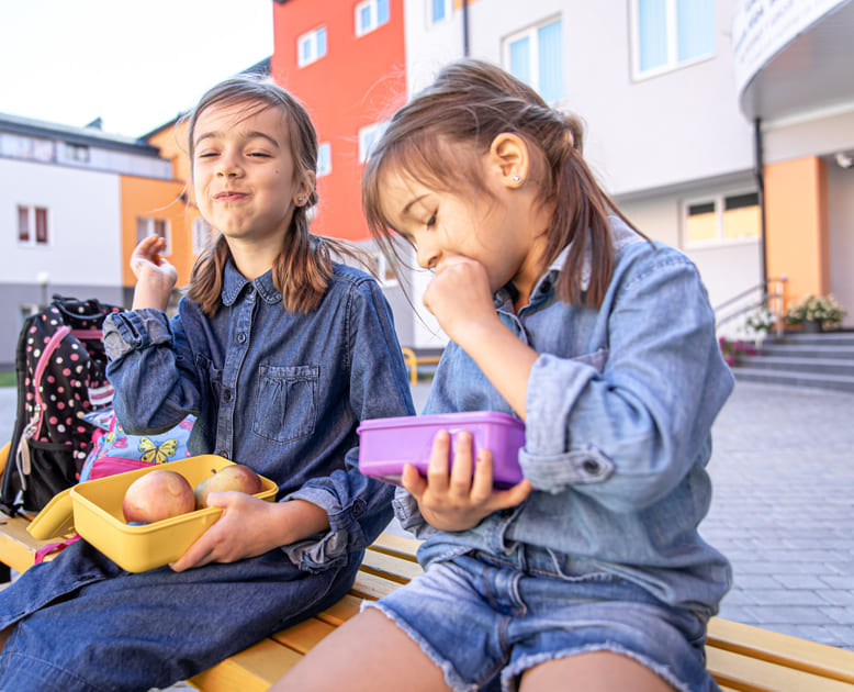 学校の屋外でお弁当箱に入ったスナックを食べながらモーニングティーを楽しむ女の子たち。