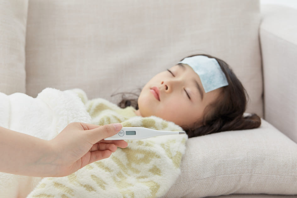 高熱でぐったり横たわる女児と体温計。