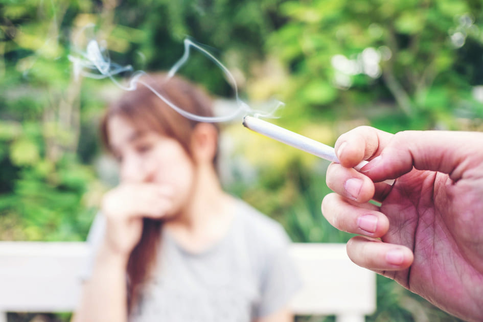 煙が出ているたばこを持つ手と、受動喫煙を嫌がっている若い女性。