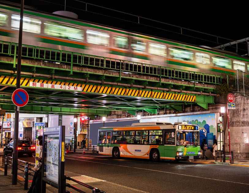 日本の交通アクセスの良さを示す、バスと電車が行きかう都心の高架下の風景。