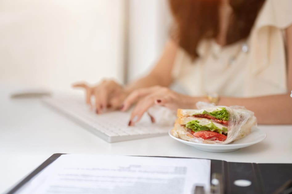 モーニングティーの時間にサンドウィッチを食べながらタイピングする女性