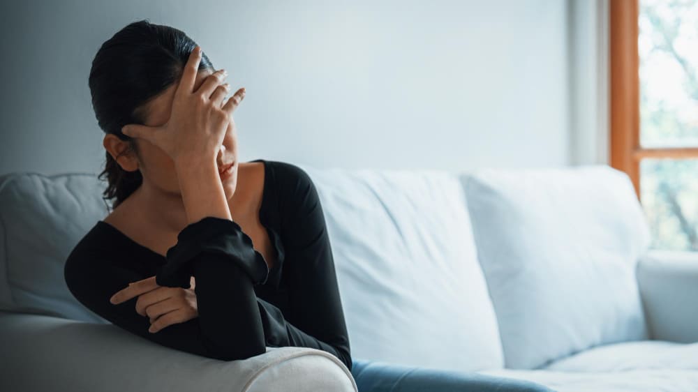 DVモラハラ夫に悩み、ソファーに座り頭を抱える妻